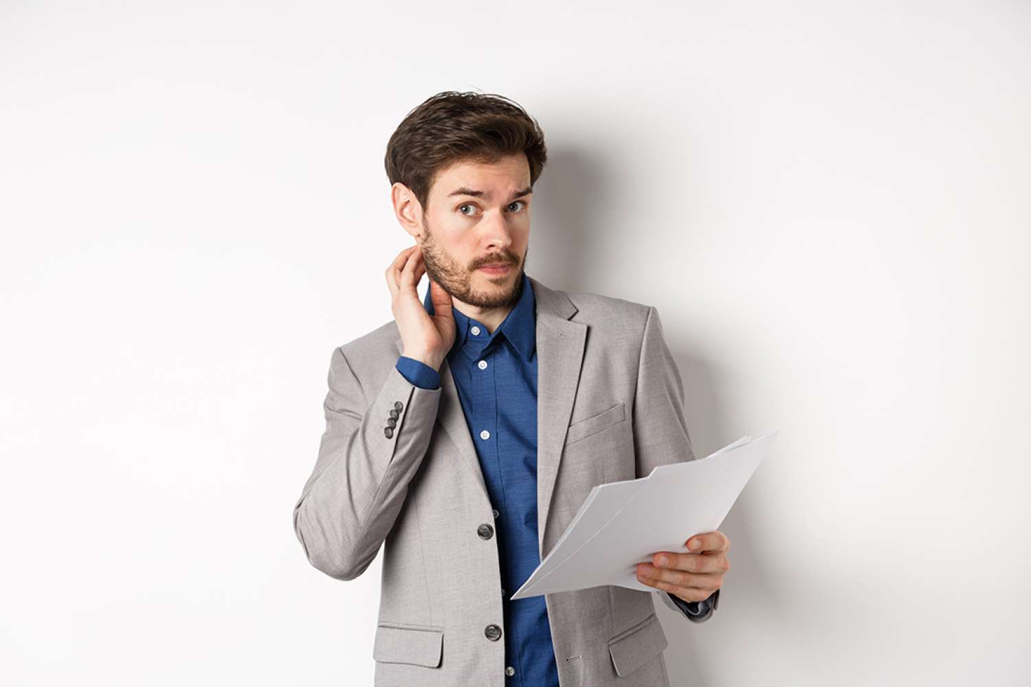 Confused office worker in suit scratching beard and look clueless, cant understand document, holding paper with indecisive face, white background.